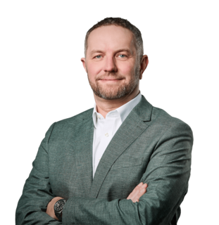 Porträt eines lächelnden Mannes im Sakko vor neutralem Hintergrund